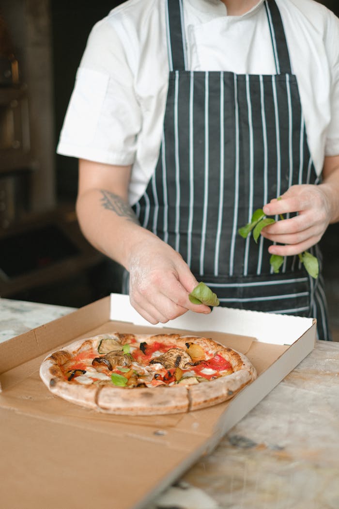 Close-up of a chef garnishing a freshly baked gourmet pizza in a kitchen setting.